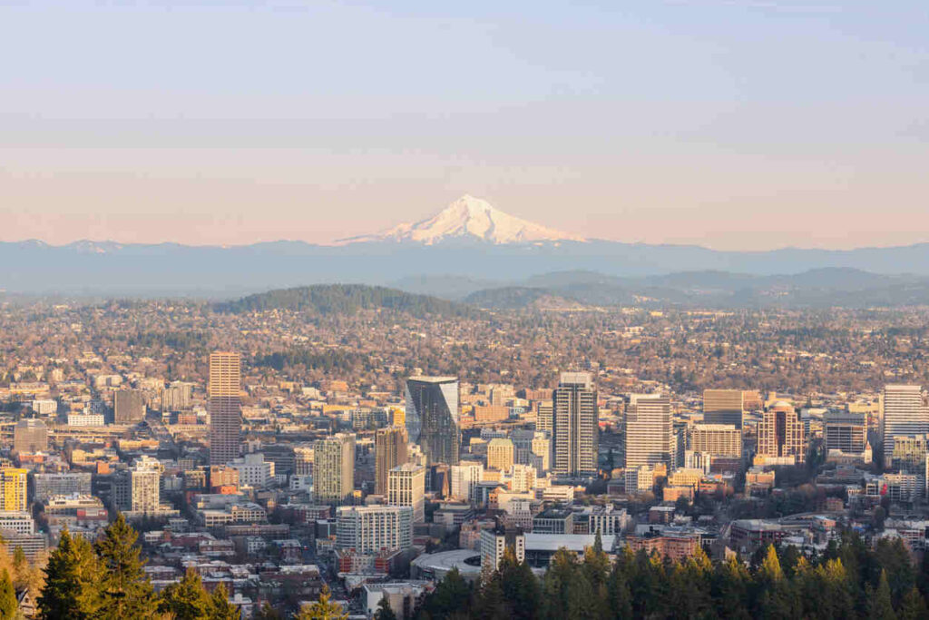 View of Portland, Oregon cityscape with Mount Hood in the background. The image shows urban buildings, highways, and the surrounding natural landscape, highlighting one of Oregon's busiest areas.