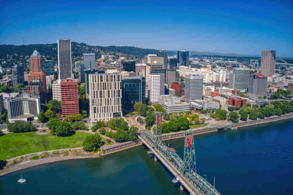 Portland city skyline with a bridge over the Willamette River, showcasing urban buildings and green parks, highlighting the downtown area.